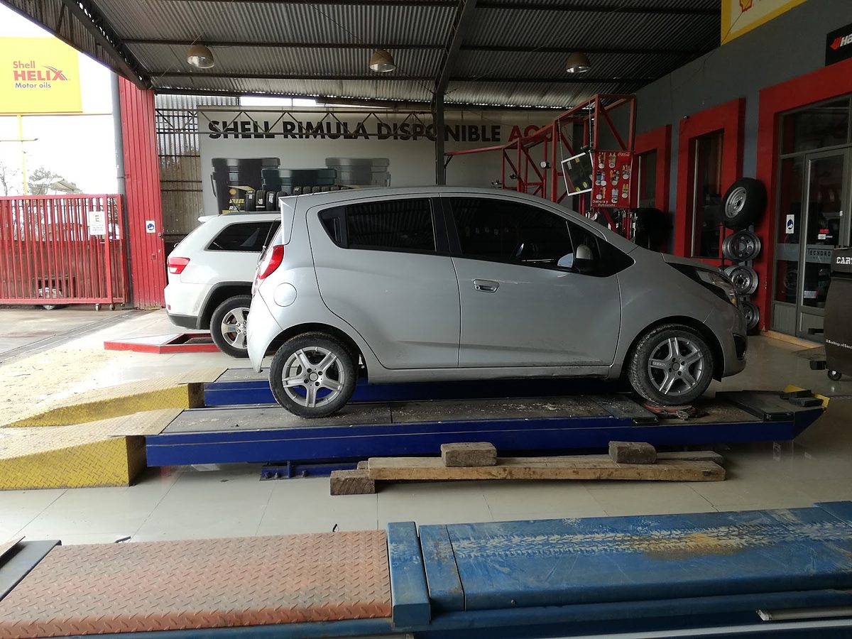 Auto sobre rampa azul de alineación, con cartel Shell Rimula al fondo y equipo Cartek a un costado.